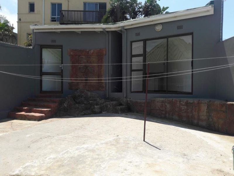 Rear exterior view featuring a concrete patio area, stone feature wall, and aluminium sliding doors leading into the property.