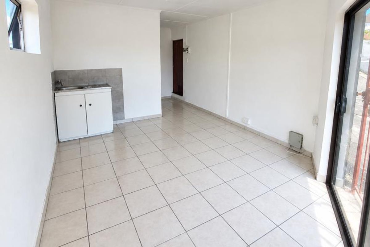 An open-plan living area featuring tiled flooring, a compact kitchenette with sink and cabinetry, and sliding glass doors leading to the exterior.