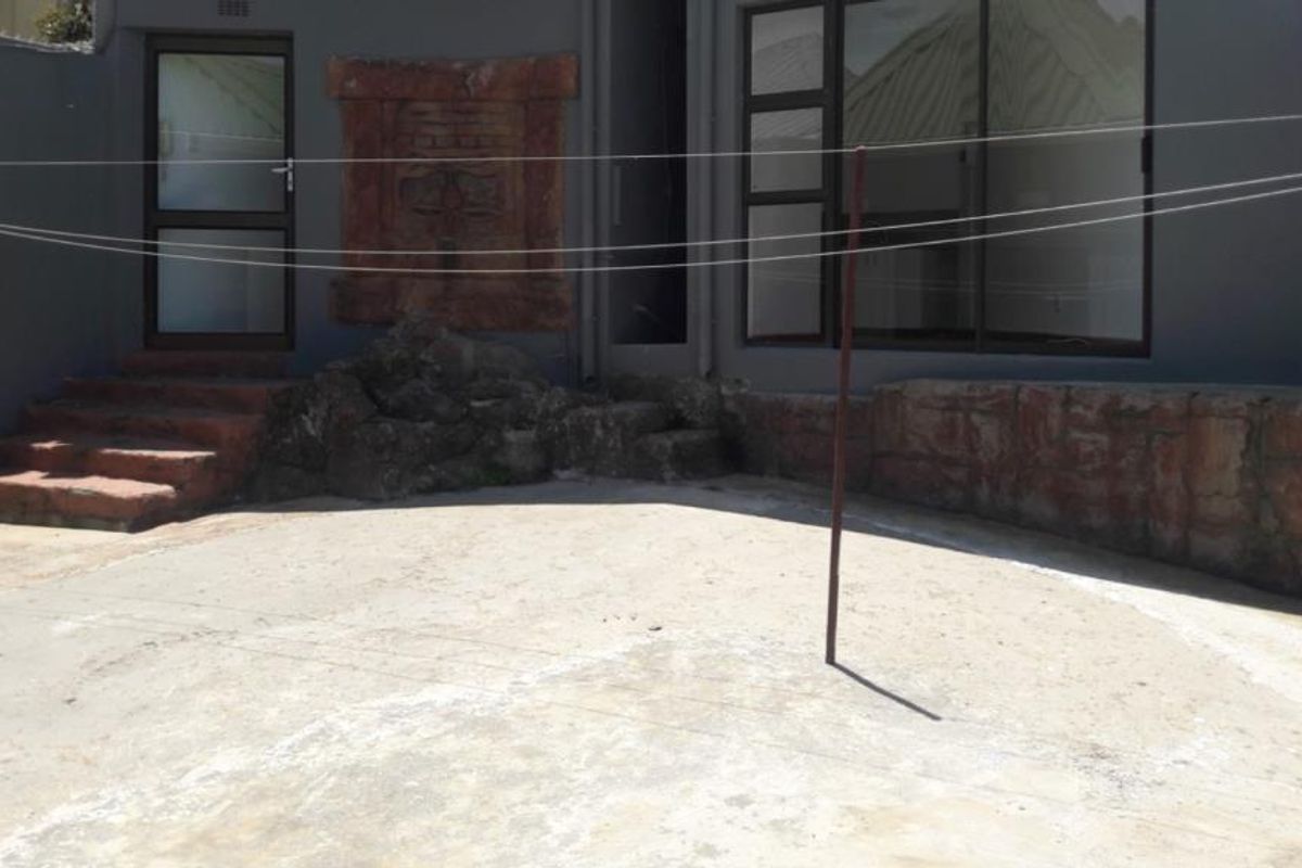 A rear exterior patio area featuring a concrete floor, stone retaining walls, and access to the interior via sliding glass and standard doors.