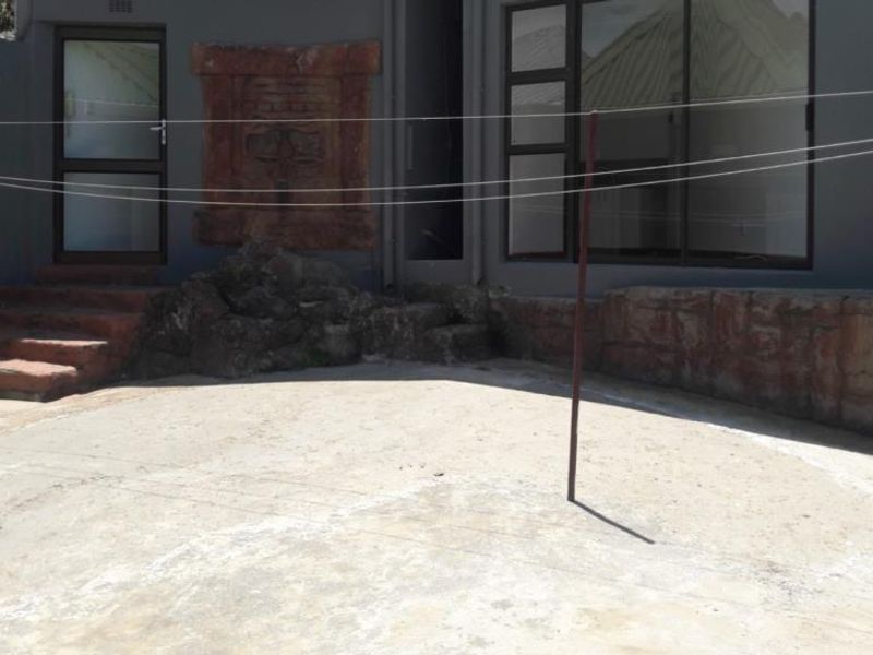 A rear exterior patio area featuring a concrete floor, stone retaining walls, and access to the interior via sliding glass and standard doors.