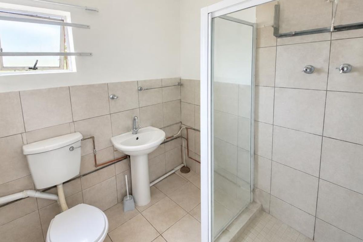A functional bathroom featuring a pedestal basin, toilet, and shower enclosure with tiled finishes and visible plumbing elements.