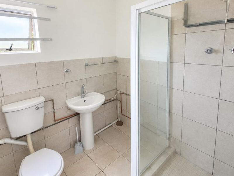 A functional bathroom featuring a pedestal basin, toilet, and shower enclosure with tiled finishes and visible plumbing elements.