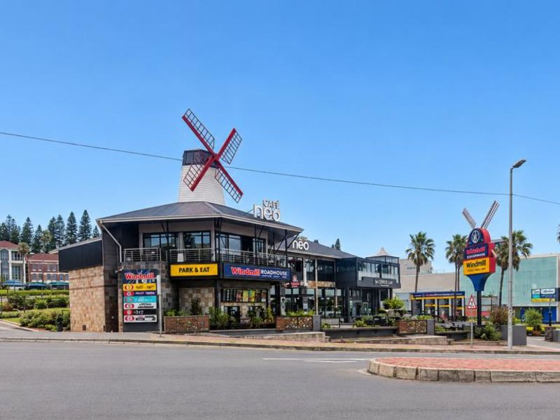 Street view of a commercial complex featuring a prominent windmill landmark, paved access roads, and surrounding landscaped areas.
