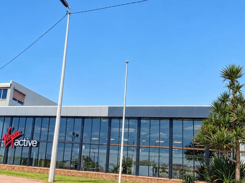 Exterior view of a modern commercial building featuring a large glass facade, metal cladding, and a brick base.