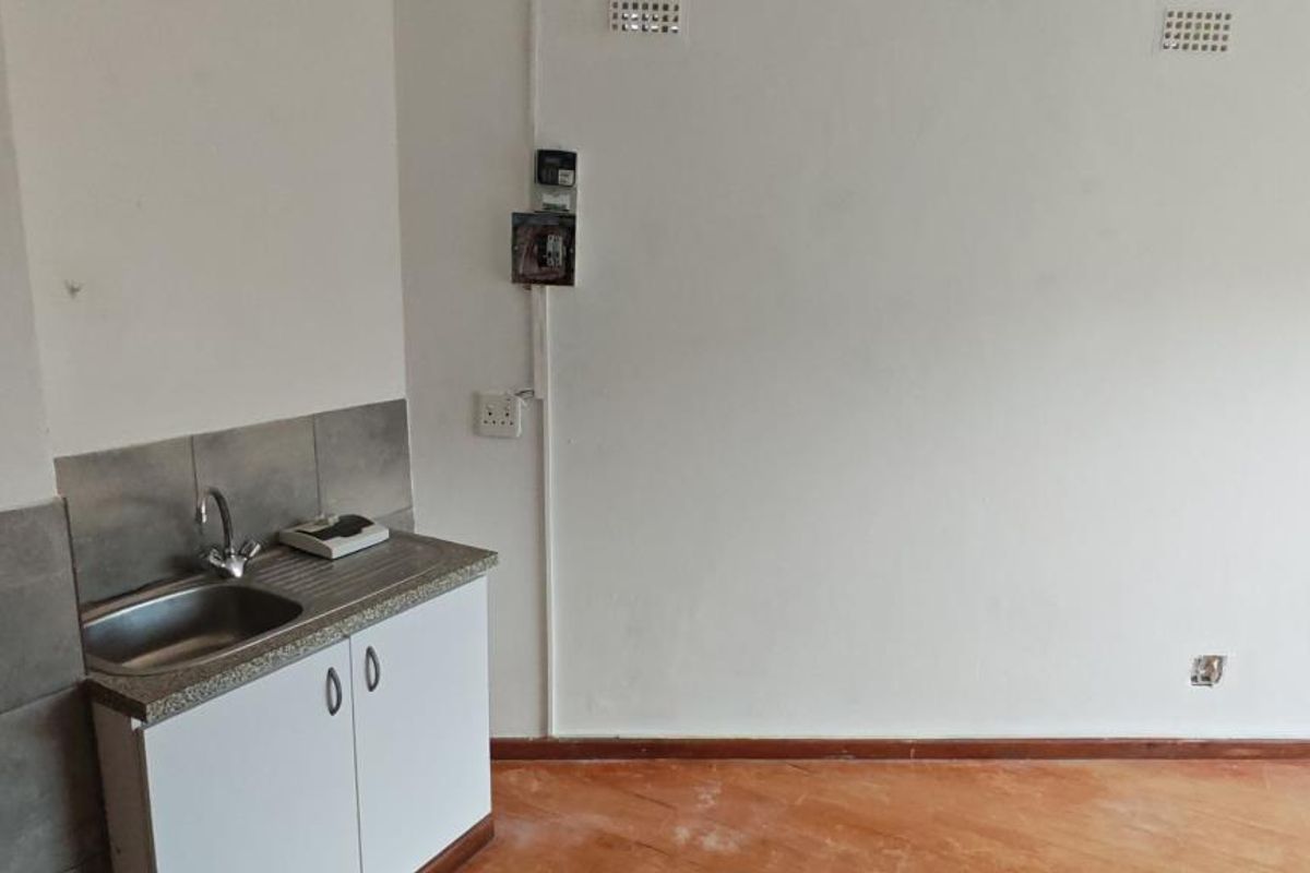 A compact, empty kitchen area featuring a single stainless steel sink, base cabinetry, and tiled backsplash, requiring cosmetic updates to improve its overall condition.