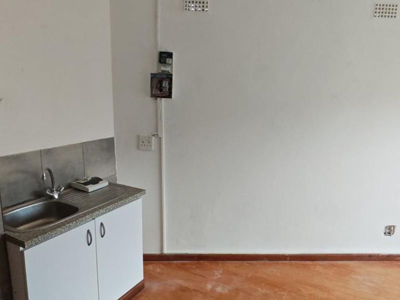 A compact, empty kitchen area featuring a single stainless steel sink, base cabinetry, and tiled backsplash, requiring cosmetic updates to improve its overall condition.