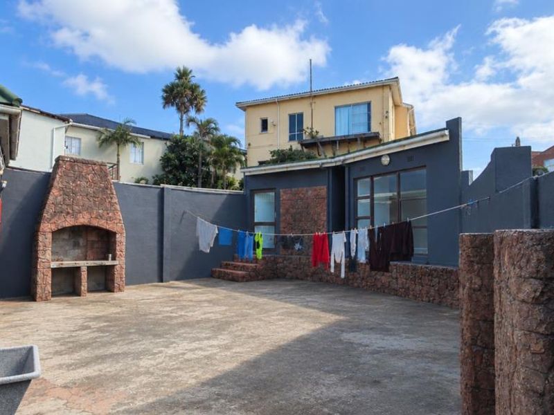 A private rear courtyard featuring a built-in stone braai, concrete paving, and perimeter walls with stone accents.