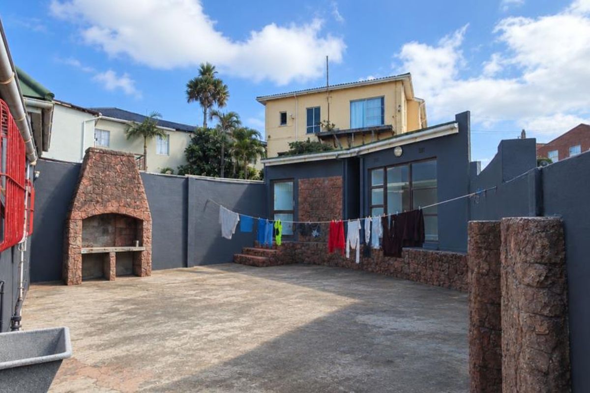 A private rear courtyard featuring a built-in stone braai, concrete paving, and perimeter walls with stone accents.