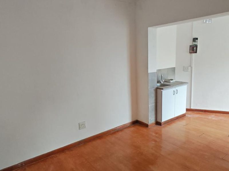 An empty open-plan living area featuring laminate flooring and a compact kitchenette with built-in cabinetry and a sink.