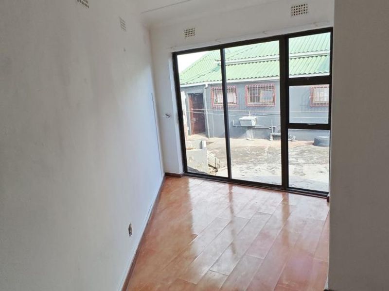 An empty living room featuring tiled flooring and a large sliding glass door providing natural light and access to the exterior.