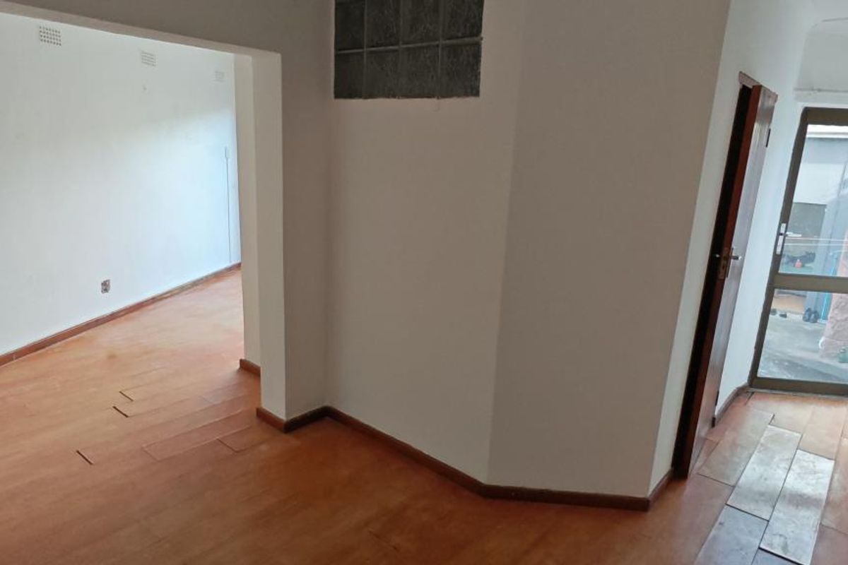 An empty living area featuring timber laminate flooring, a glass block feature window, and an aluminium framed glass door leading to an exterior space.