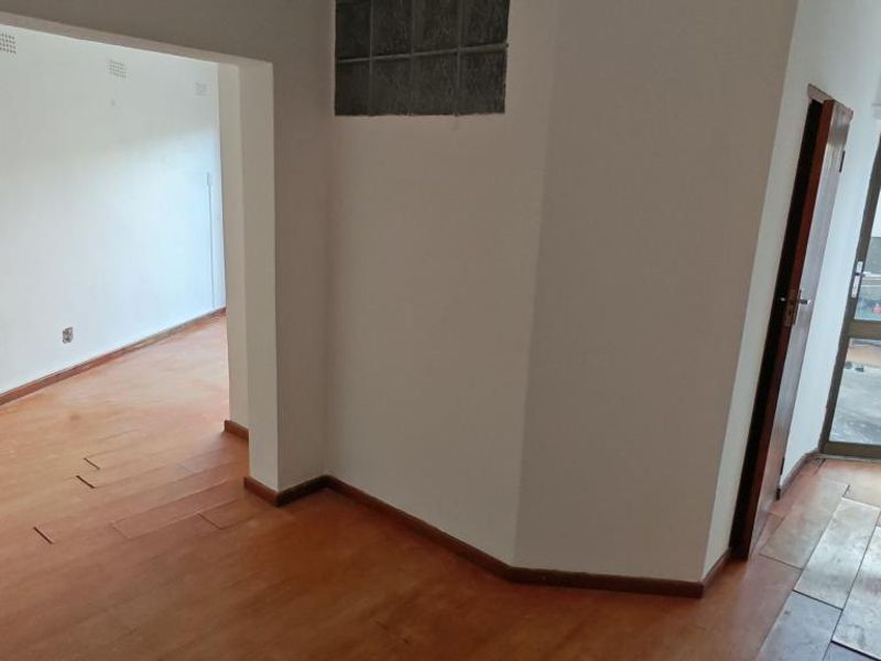 An empty living area featuring timber laminate flooring, a glass block feature window, and an aluminium framed glass door leading to an exterior space.