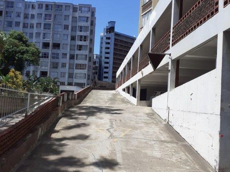 An exterior view of the apartment complex driveway and parking structure, showing concrete surfaces and surrounding residential building facades.
