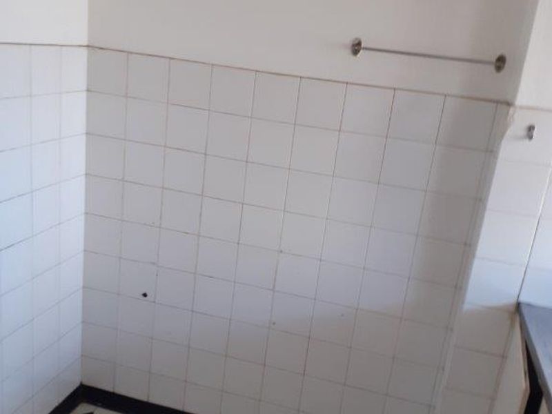A vacant kitchen corner featuring classic patterned floor tiles, a tiled splashback, and a wall-mounted electrical distribution board.