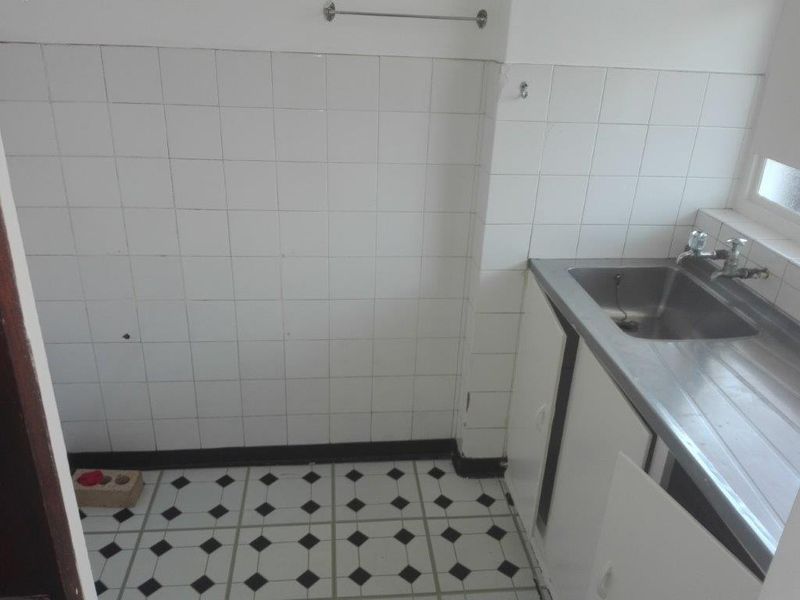 A compact kitchen area featuring a stainless steel sink, tiled splashback, and patterned floor tiles, requiring some maintenance and cosmetic updates.