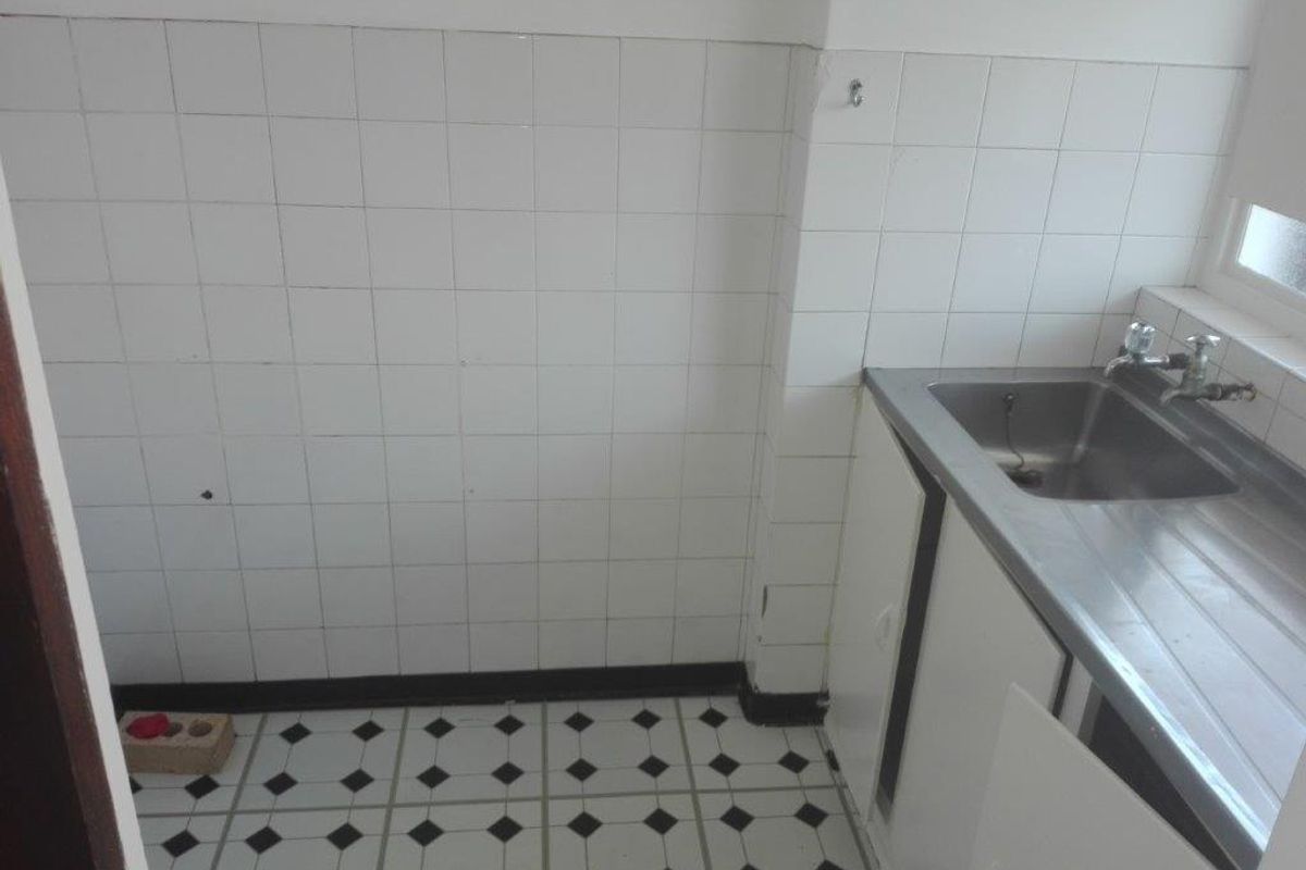 A compact kitchen area featuring a stainless steel sink, tiled splashback, and patterned floor tiles, requiring some maintenance and cosmetic updates.