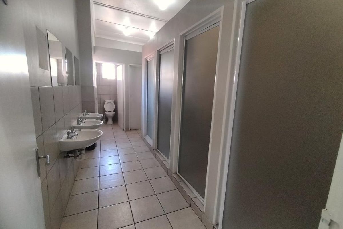 A communal bathroom facility featuring multiple wall-mounted washbasins, tiled flooring, and private cubicle doors.