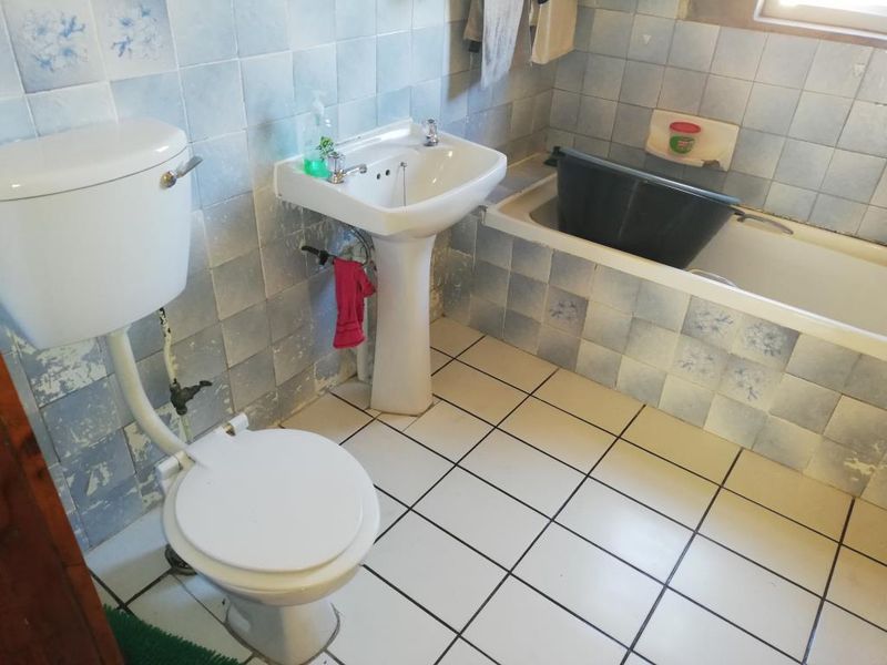 A dated bathroom featuring a pedestal basin, toilet, and bathtub with blue patterned wall tiles and white floor tiles.