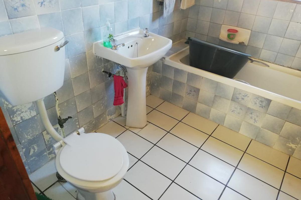 A dated bathroom featuring a pedestal basin, toilet, and bathtub with blue patterned wall tiles and white floor tiles.