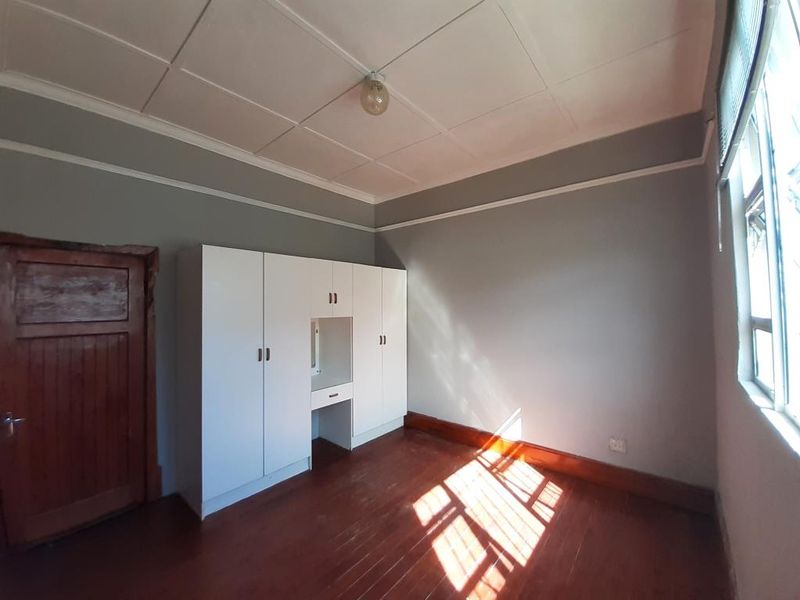 A bright, empty bedroom featuring original wooden flooring, built-in white cabinetry, and classic ceiling tiles, offering a clean canvas for personalization.