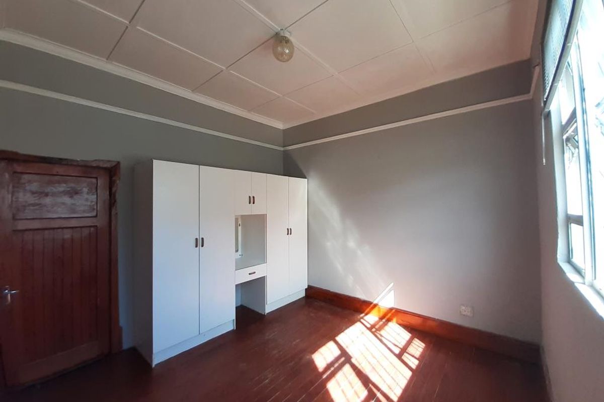A bright, empty bedroom featuring original wooden flooring, built-in white cabinetry, and classic ceiling tiles, offering a clean canvas for personalization.