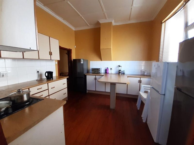 A dated kitchen featuring timber flooring, laminate countertops, tiled backsplash, and built-in cabinetry with an integrated extractor fan housing.