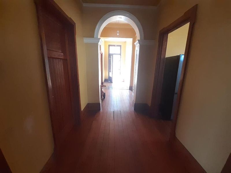 A long hallway featuring original timber flooring and a classic architectural archway, connecting multiple rooms within the apartment.