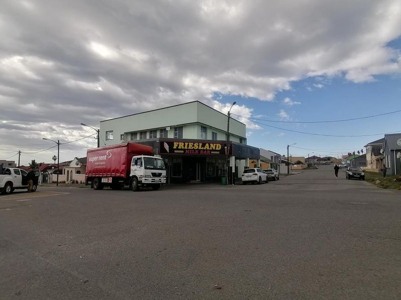 Street view of a corner commercial building featuring Friesland Milk Bar signage, situated on a paved road with surrounding residential properties.