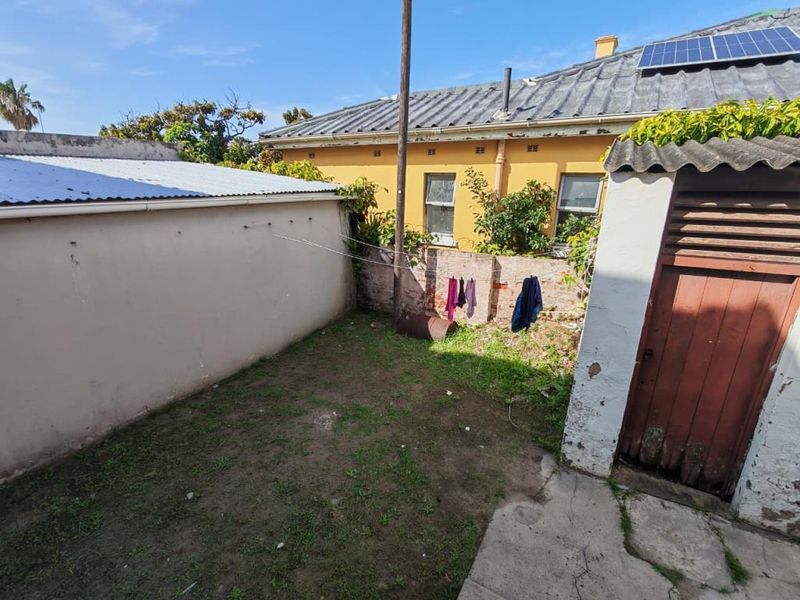 Rear courtyard area featuring a small patch of lawn, concrete paving, and access to the main building with visible solar panels on the roof.