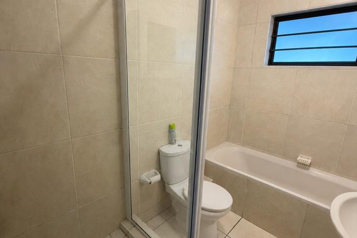 A functional bathroom featuring a glass-enclosed shower, a built-in bathtub, a toilet, and neutral floor-to-ceiling wall tiling.