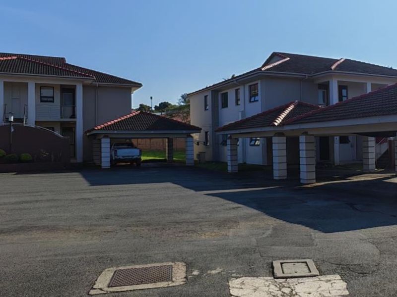 Exterior view of a townhouse complex featuring multiple covered parking bays, tiled roofing, and a paved driveway area.