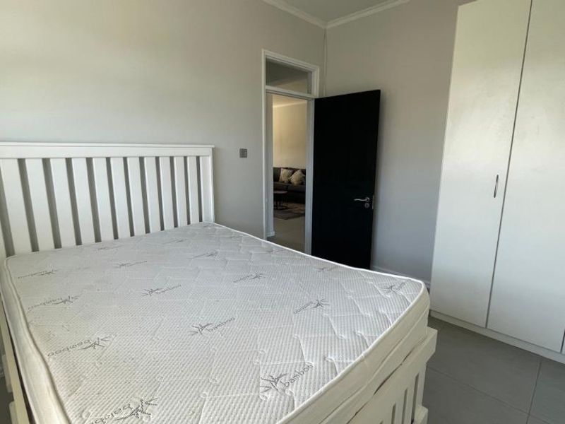 A bright bedroom featuring neutral walls, tiled flooring, and a large built-in wardrobe, offering a clean and functional living space.