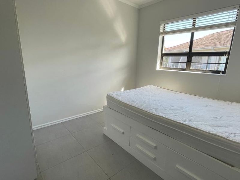 A bright bedroom featuring neutral tiled flooring, a built-in cupboard, and an aluminium-framed window with fitted blinds.