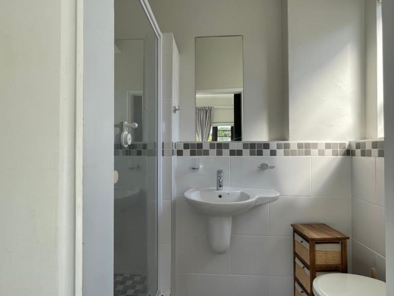 A functional bathroom featuring a pedestal basin, chrome mixer tap, tiled splashback, and a glass shower enclosure.
