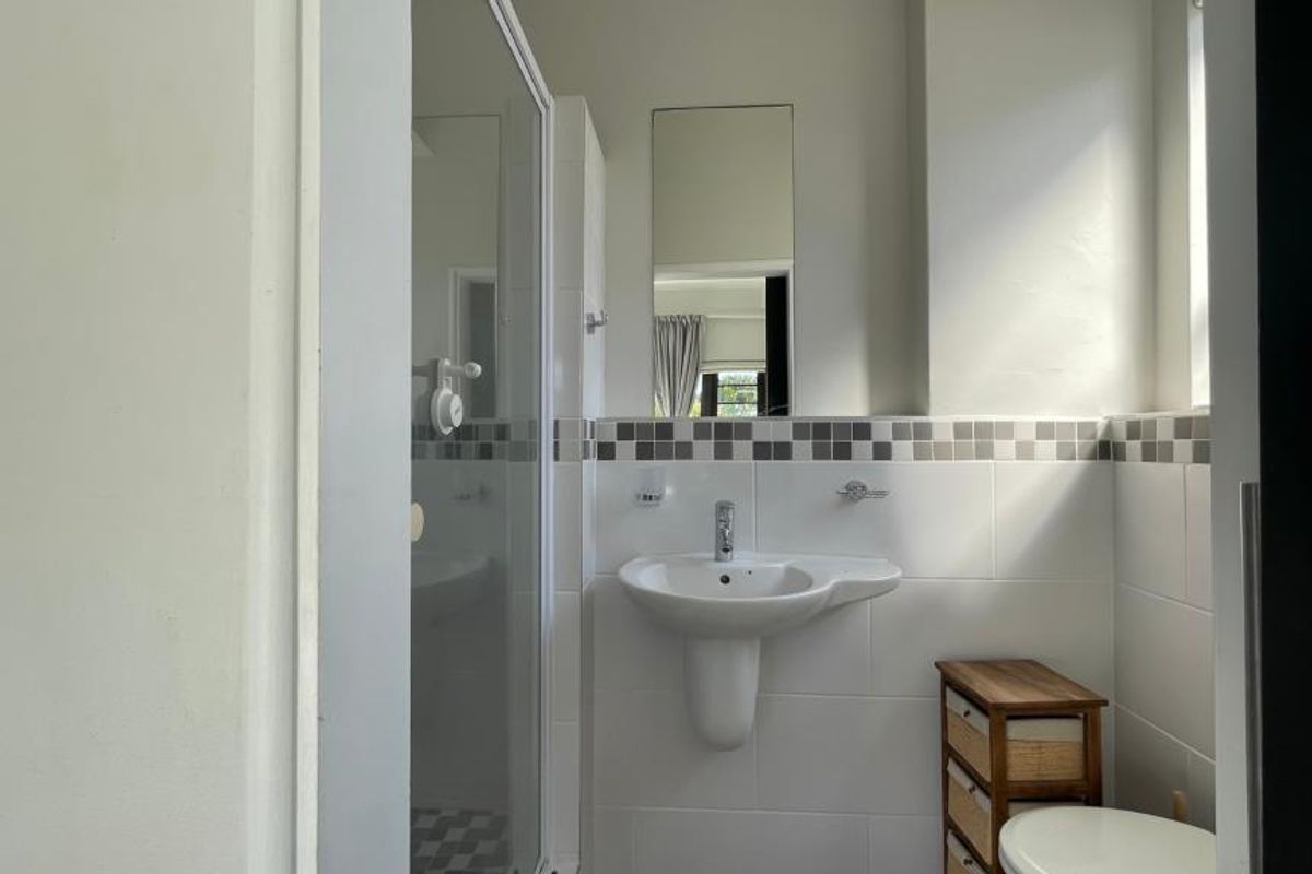 A functional bathroom featuring a pedestal basin, chrome mixer tap, tiled splashback, and a glass shower enclosure.