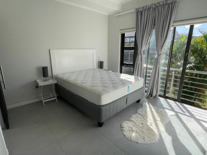 A bright bedroom featuring tiled flooring, a built-in wardrobe, and large sliding glass doors providing access to a balcony with garden views.