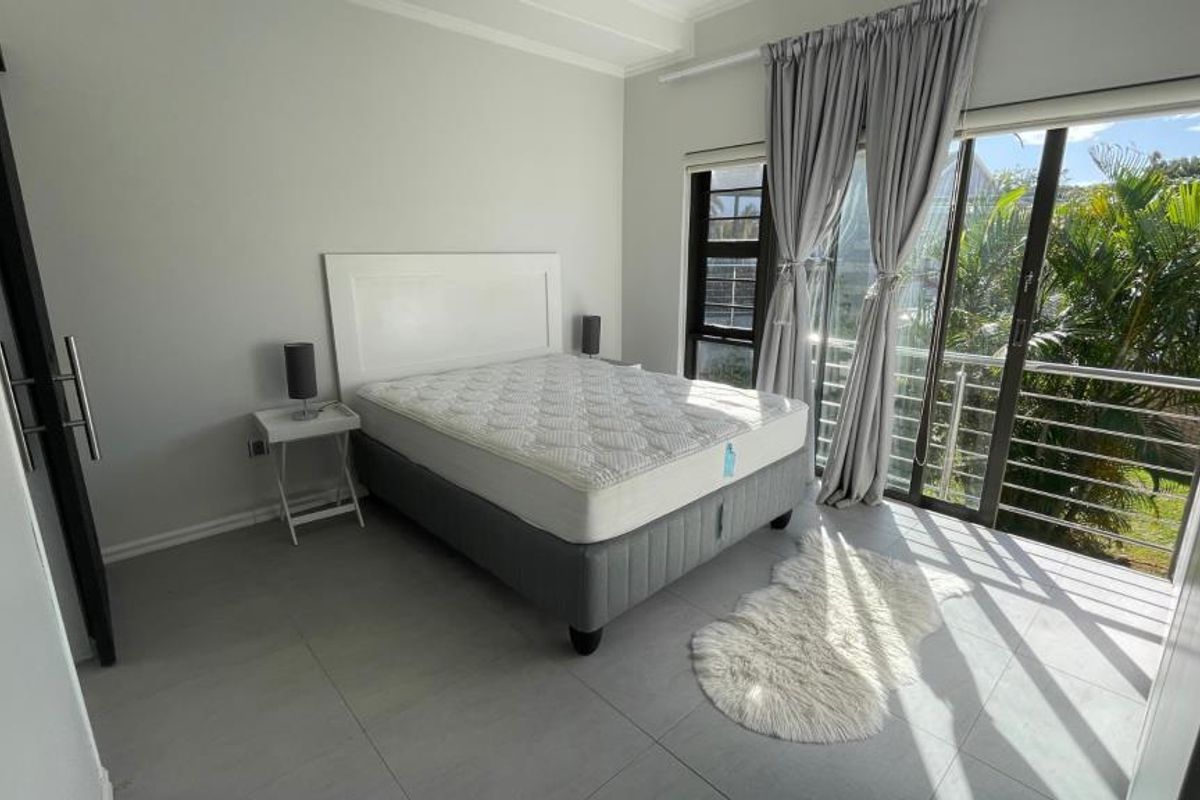 A bright bedroom featuring tiled flooring, a built-in wardrobe, and large sliding glass doors providing access to a balcony with garden views.