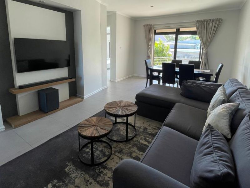 Spacious open-plan living and dining area featuring a modern built-in media wall, tiled flooring, and large sliding doors leading to an outdoor space.