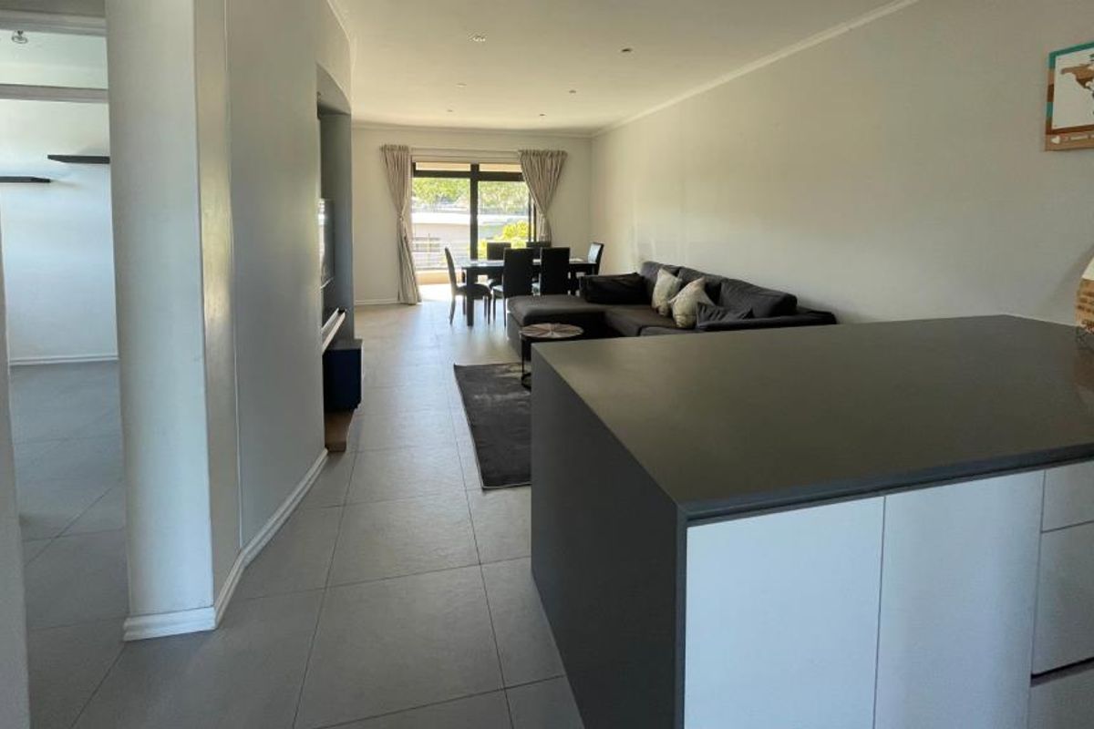 Spacious open-plan living area featuring a modern kitchen island, neutral tiled flooring, and seamless flow to the dining space and outdoor access.