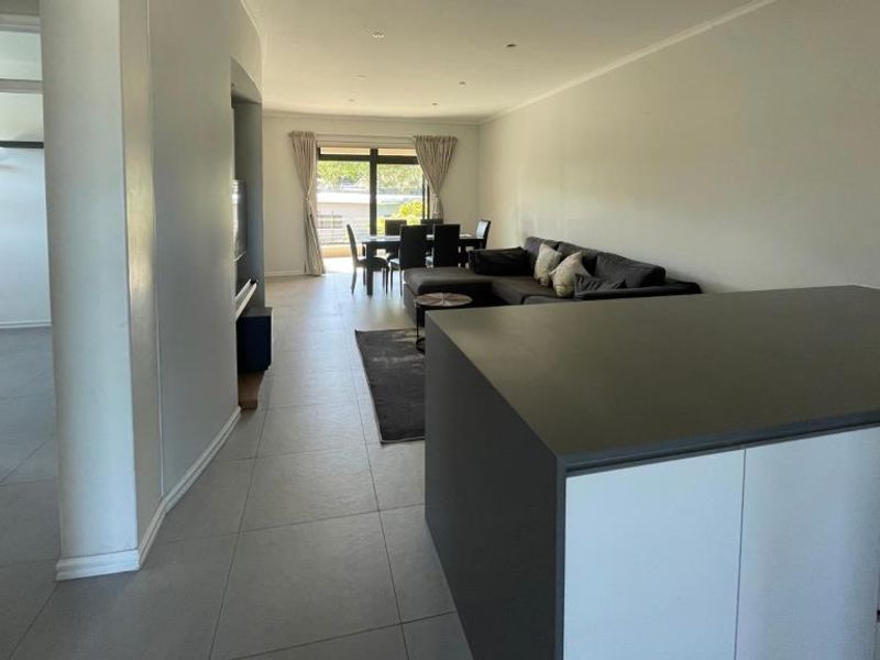 Spacious open-plan living area featuring a modern kitchen island, neutral tiled flooring, and seamless flow to the dining space and outdoor access.