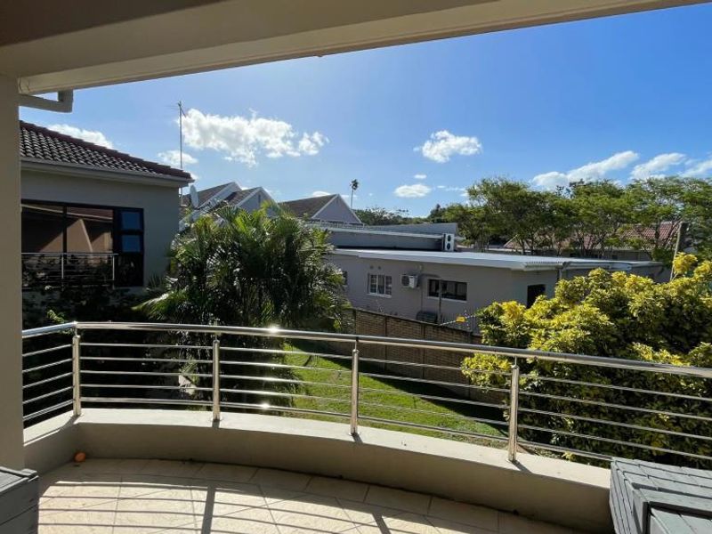 A covered balcony featuring a stainless steel balustrade and tiled flooring, offering an elevated view of the surrounding residential area.