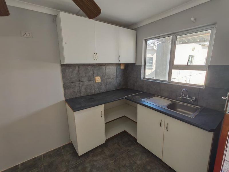 A compact kitchen featuring built-in cabinetry, dark tiled backsplash, laminate countertops, and a stainless steel sink, currently in need of minor repairs.