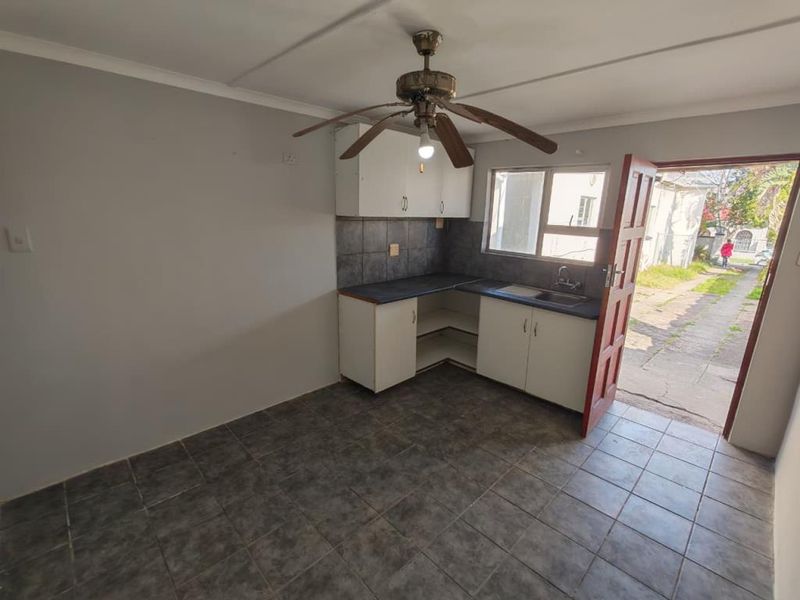 A functional kitchen area featuring tiled flooring, built-in cabinetry with laminate countertops, a stainless steel sink, and direct access to the exterior.