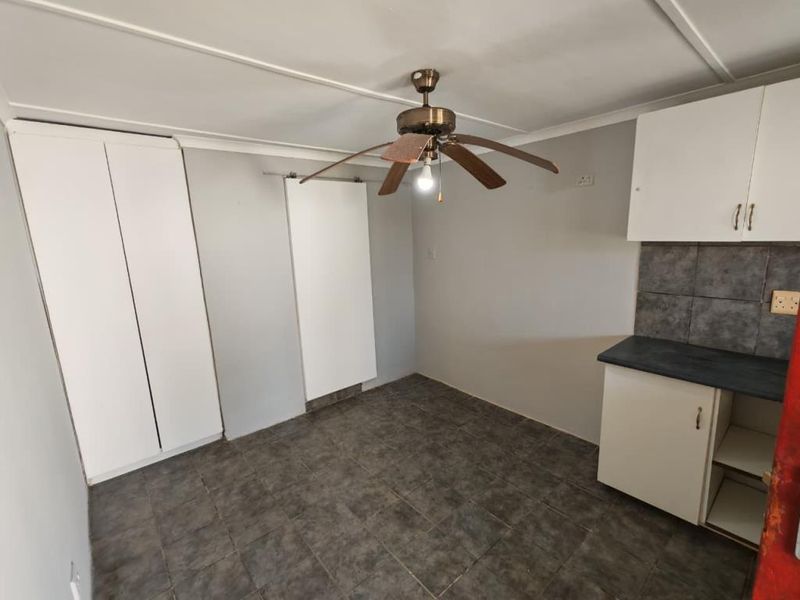A functional kitchen area featuring tiled flooring, built-in cabinetry, a tiled backsplash, and a ceiling fan.
