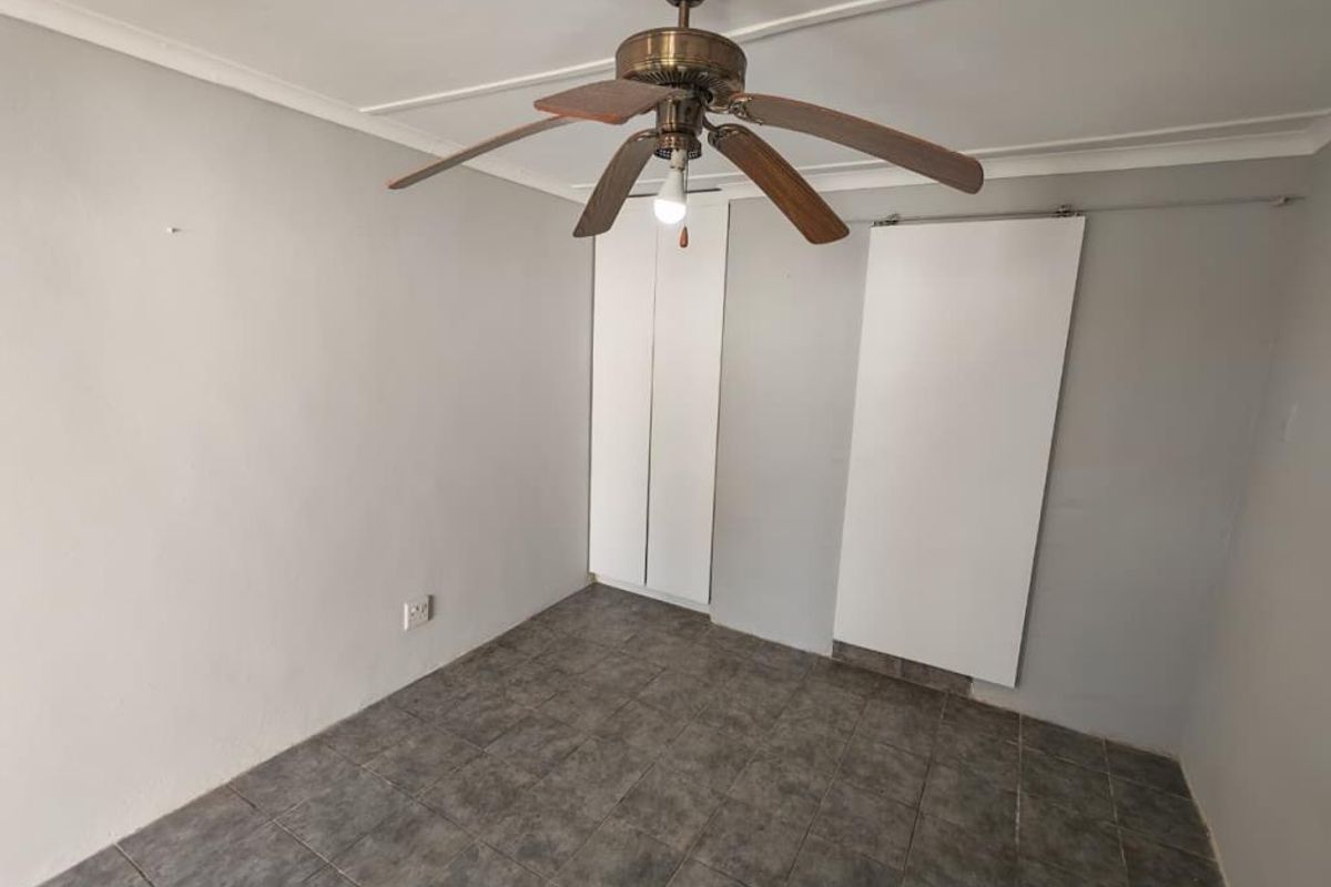 An empty bedroom featuring tiled flooring, a ceiling fan, and built-in cupboards, providing a blank canvas for potential updates.