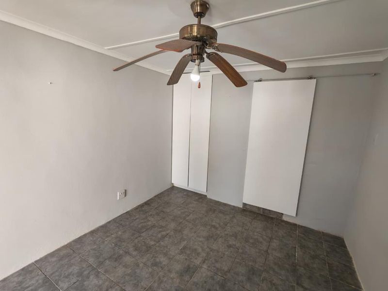 An empty bedroom featuring tiled flooring, a ceiling fan, and built-in cupboards, providing a blank canvas for potential updates.