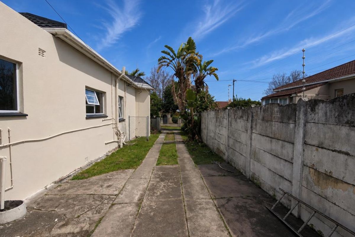 Rear exterior view of the property featuring a concrete driveway, precast boundary wall with electric fencing, and access to the side of the building.