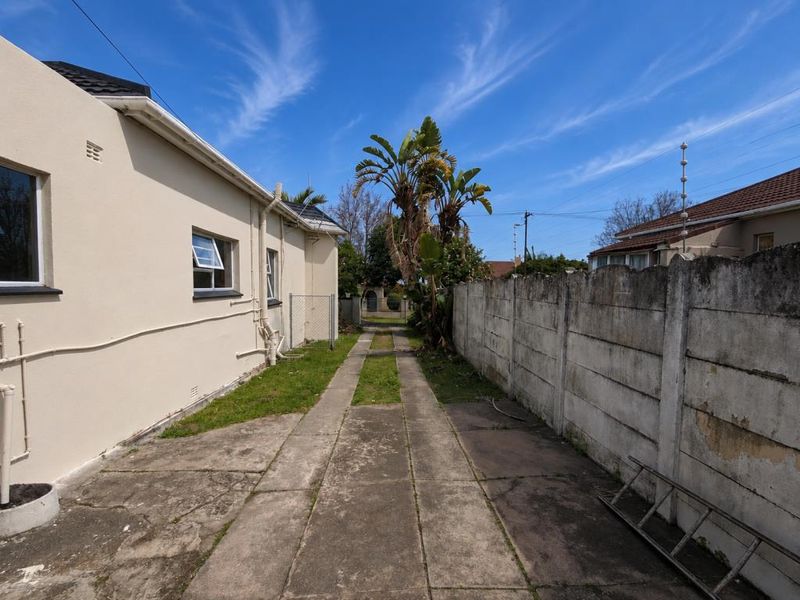 Rear exterior view of the property featuring a concrete driveway, precast boundary wall with electric fencing, and access to the side of the building.
