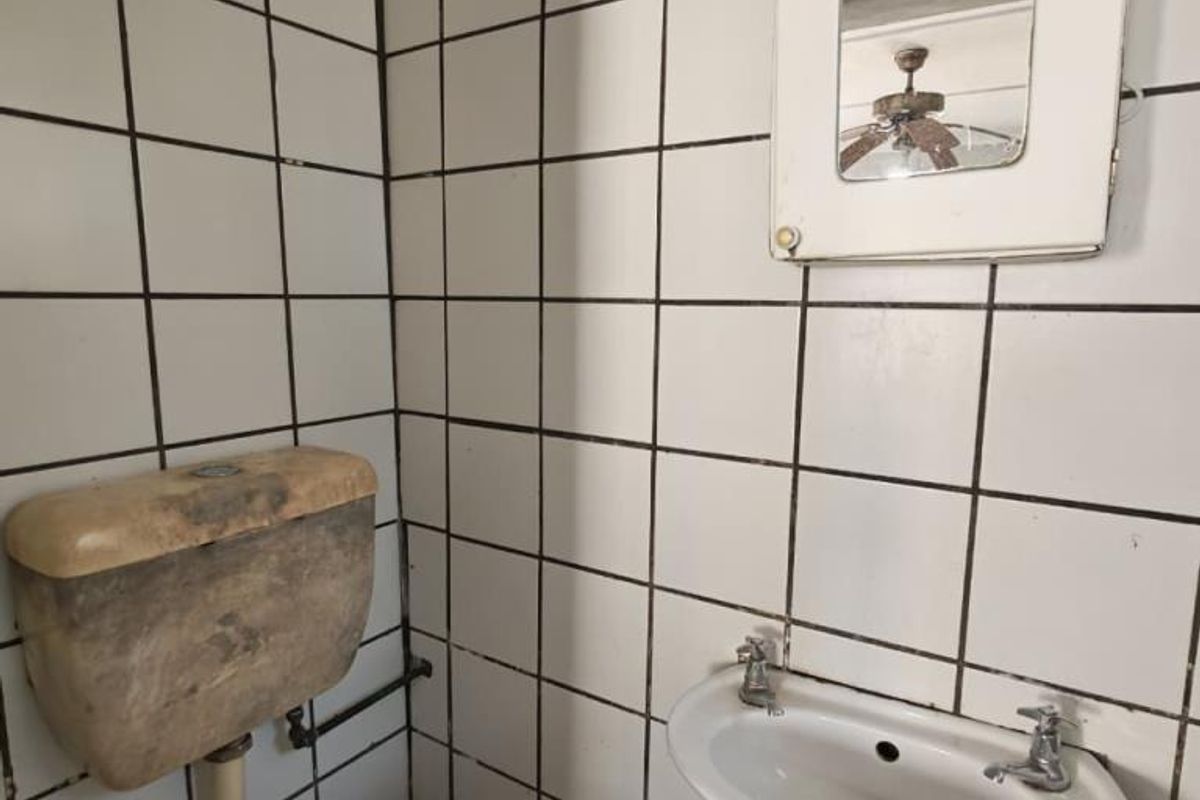 A compact bathroom featuring tiled walls, a wall-mounted basin, and a toilet with a dated cistern, requiring modernization and cosmetic updates.