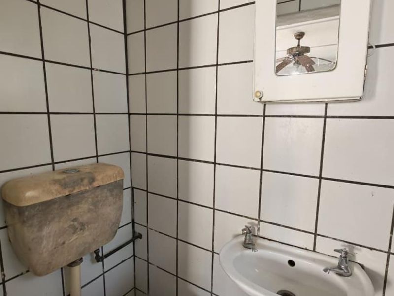 A compact bathroom featuring tiled walls, a wall-mounted basin, and a toilet with a dated cistern, requiring modernization and cosmetic updates.